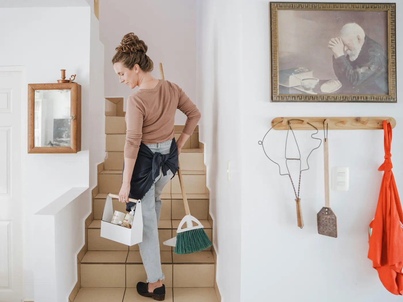 Domestic cleaner carrying a cleaning caddy and brush up the stairs of a family home