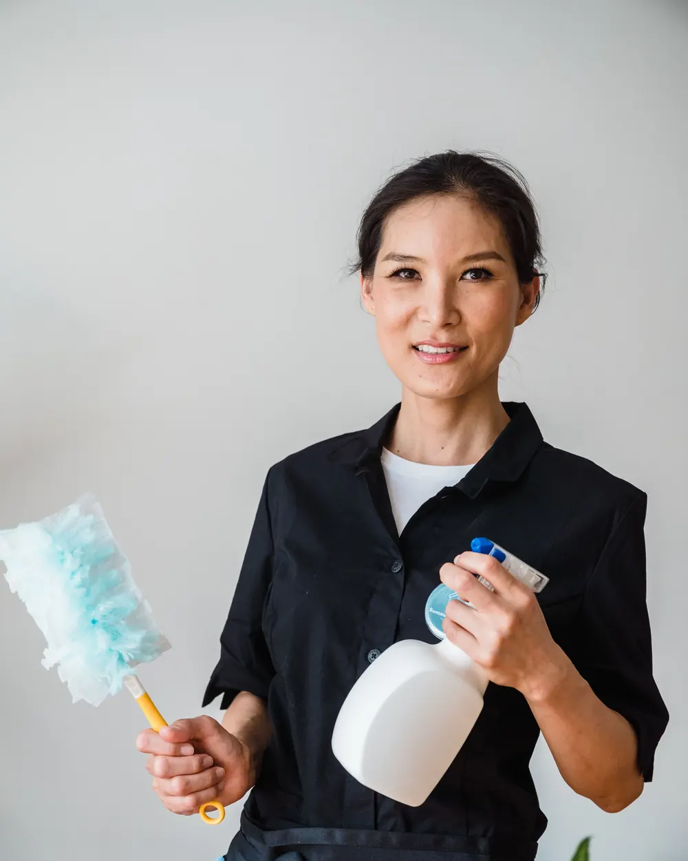 Friendly professional cleaner holding a duster and spray bottle
