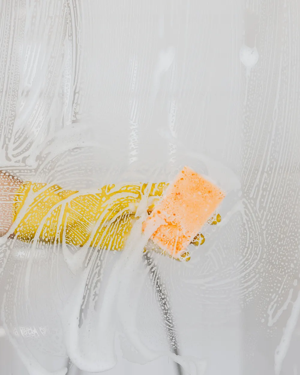 Glass shower screen being scrubbed with a sponge