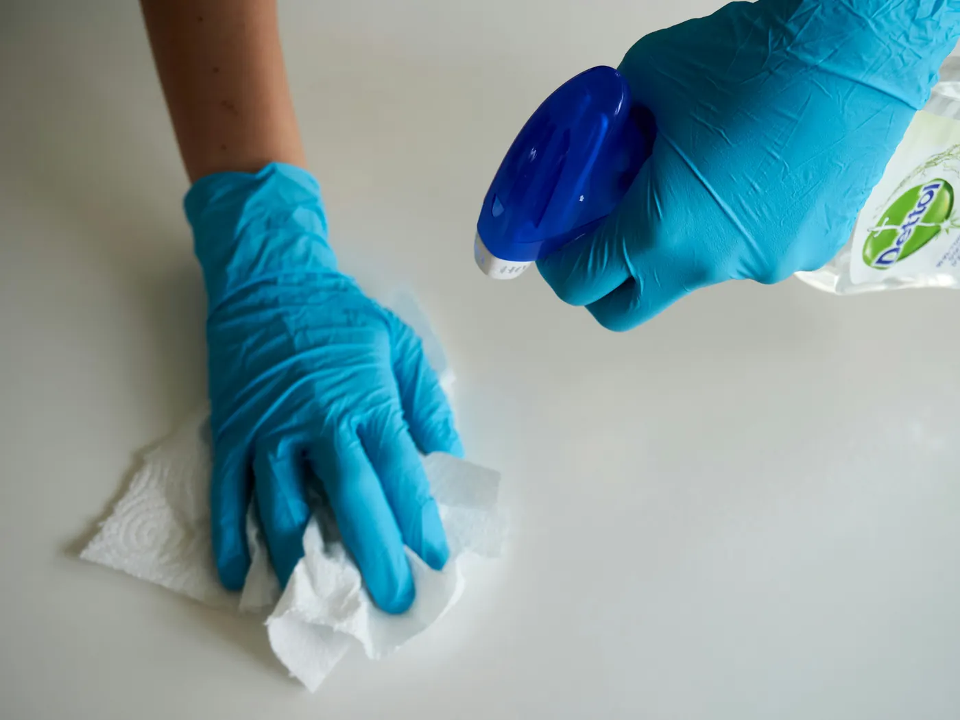 Gloved hands spraying and wiping a white surface clean